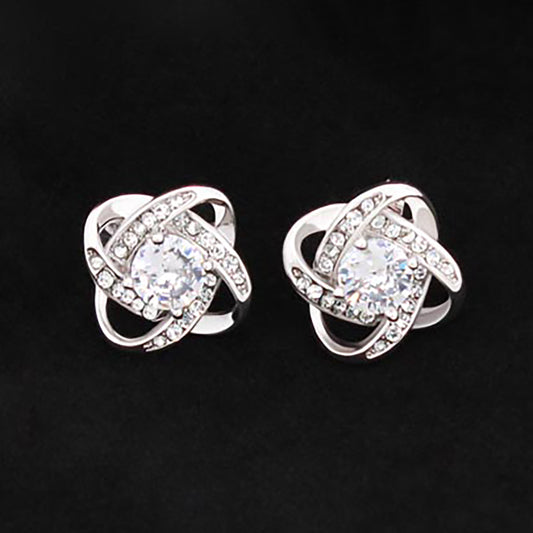“Love Knot stud earrings with a central round cubic zirconia and surrounding crystal‑encrusted knot design in 14K white‑gold‑plated stainless steel.”